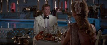 Movie still from “Octopussy” (1983), directed by John Glen – A man in a white tuxedo sitting at a table with a woman; Medium shot, Over the shoulder angle