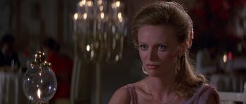 Movie still from “Octopussy” (1983), directed by John Glen – A woman in a purple dress is looking at the camera; Close Up shot, Over the shoulder angle