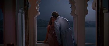 Movie still from “Octopussy” (1983), directed by John Glen – A man and a woman standing next to each other in front of a lake; Medium shot, Low angle