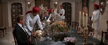 Movie still from “Octopussy” (1983), directed by John Glen – A group of people standing around a dining room table; Wide shot, High angle