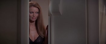 Movie still from “Octopussy” (1983), directed by John Glen – A woman in a black bra is posing for a picture; Close Up shot, Over the shoulder angle