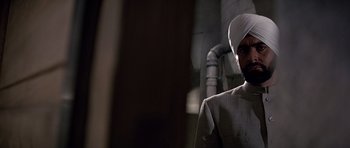 Movie still from “Octopussy” (1983), directed by John Glen – A man with a white turban is standing in a room; Close Up shot, Low angle