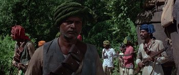 Movie still from “Octopussy” (1983), directed by John Glen – A group of men standing next to each other on a lush green field; Medium shot, Over the shoulder angle