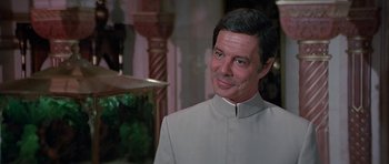 Movie still from “Octopussy” (1983), directed by John Glen – A man in a white suit smiling for the camera; Close Up shot, Over the shoulder angle