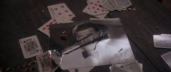 Movie still from “Octopussy” (1983), directed by John Glen – An old photo of a man holding a knife in his mouth; Extreme Close Up shot, Overhead angle