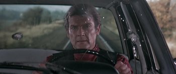 Movie still from “Octopussy” (1983), directed by John Glen – A person driving a car; Close Up shot, Over the shoulder angle
