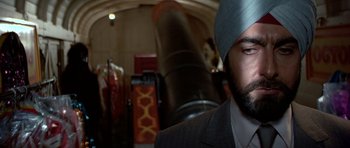 Movie still from “Octopussy” (1983), directed by John Glen – A man in a suit and turban standing in front of a large object; Close Up shot, Over the shoulder angle