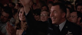 Movie still from “Octopussy” (1983), directed by John Glen – A group of people sitting in front of a crowd of people; Close Up shot, Low angle