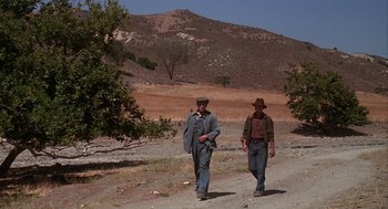 Movie still from “Of Mice and Men” (1992), directed by Gary Sinise – Two men walking down a dirt road near some trees; Wide shot, Low angle
