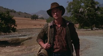 Movie still from “Of Mice and Men” (1992), directed by Gary Sinise – A man in a hat and a jacket standing in a field; Medium shot, Over the shoulder angle