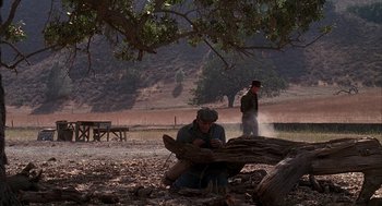 Movie still from “Of Mice and Men” (1992), directed by Gary Sinise – A man sitting on the ground next to a tree; Wide shot, High angle