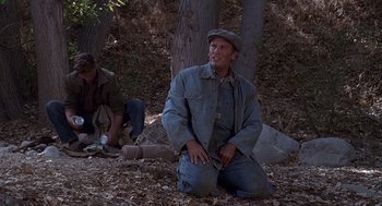 Movie still from “Of Mice and Men” (1992), directed by Gary Sinise – A man sitting on the ground in the woods; Medium shot, High angle