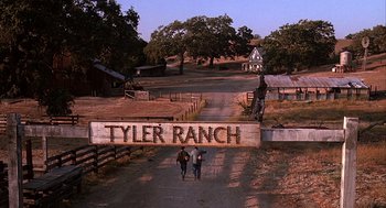 Movie still from “Of Mice and Men” (1992), directed by Gary Sinise – Two people walking down a dirt road near a wooden sign; Wide shot, Low angle
