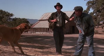Movie still from “Of Mice and Men” (1992), directed by Gary Sinise – A man in a hat is walking with a dog; Wide shot, Low angle