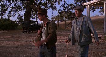 Movie still from “Of Mice and Men” (1992), directed by Gary Sinise – Two men are walking in the dirt near an old car; Medium shot, Low angle