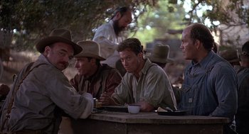 Movie still from “Of Mice and Men” (1992), directed by Gary Sinise – A group of men sitting at a table with food; Medium shot, Over the shoulder angle