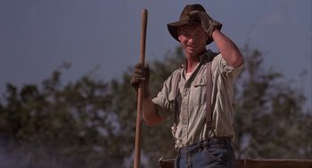 Movie still from “Of Mice and Men” (1992), directed by Gary Sinise – A man holding a wooden stick wearing a hat; Medium shot, Low angle