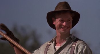 Movie still from “Of Mice and Men” (1992), directed by Gary Sinise – A man wearing a hat and holding a wooden stick; Close Up shot, Low angle