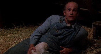 Movie still from “Of Mice and Men” (1992), directed by Gary Sinise – A man holding an animal while sitting on the ground; Medium shot, Low angle