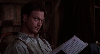 Movie still from “Of Mice and Men” (1992), directed by Gary Sinise – A man sitting in a chair holding an open book; Close Up shot, Low angle
