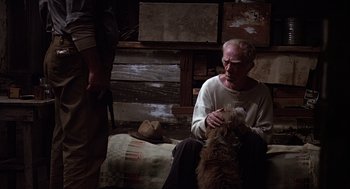 Movie still from “Of Mice and Men” (1992), directed by Gary Sinise – An old man sitting on the ground petting a dog; Medium shot, High angle
