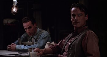Movie still from “Of Mice and Men” (1992), directed by Gary Sinise – Two men sitting at a table with a cup of coffee; Medium shot, Low angle