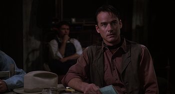 Movie still from “Of Mice and Men” (1992), directed by Gary Sinise – A man sitting at a table with a book in his hand; Medium shot, Over the shoulder angle