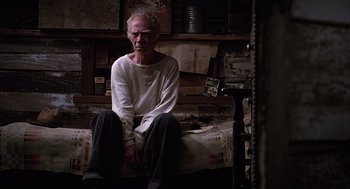 Movie still from “Of Mice and Men” (1992), directed by Gary Sinise – An older man sitting on a bed in a room; Medium shot, High angle