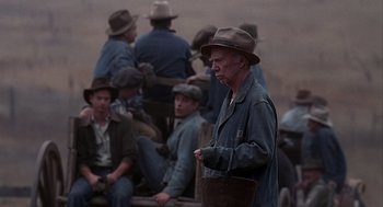 Movie still from “Of Mice and Men” (1992), directed by Gary Sinise – An old man wearing a hat standing in front of a group of men; Medium shot, High angle