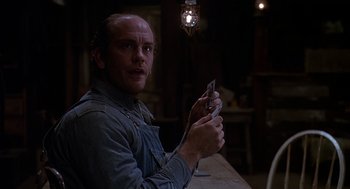 Movie still from “Of Mice and Men” (1992), directed by Gary Sinise – A man sitting at a table holding a cell phone in his hand; Close Up shot, Over the shoulder angle