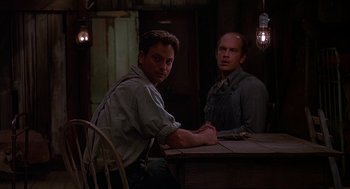 Movie still from “Of Mice and Men” (1992), directed by Gary Sinise – A man sitting at a table next to another man; Medium shot, Low angle
