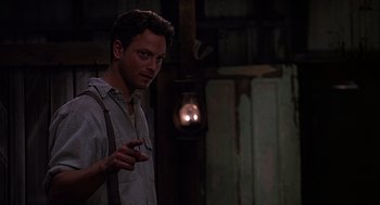 Movie still from “Of Mice and Men” (1992), directed by Gary Sinise – A man standing in front of a light in a dark room; Medium shot, Over the shoulder angle