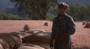 Movie still from “Of Mice and Men” (1992), directed by Gary Sinise – A man standing in front of a pile of burlap bags; Medium shot, Over the shoulder angle