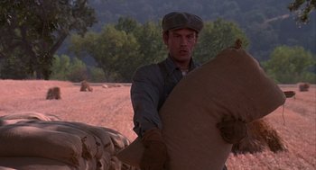 Movie still from “Of Mice and Men” (1992), directed by Gary Sinise – A man holding a bag while standing in a field; Medium shot, Low angle