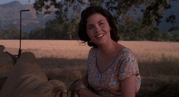 Movie still from “Of Mice and Men” (1992), directed by Gary Sinise – A woman sitting in a field smiling for the camera; Close Up shot, Over the shoulder angle