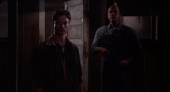 Movie still from “Of Mice and Men” (1992), directed by Gary Sinise – Two men standing next to each other in a dark room; Medium shot, Over the shoulder angle