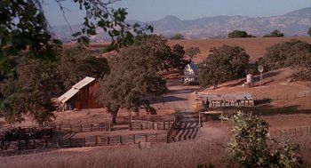Movie still from “Of Mice and Men” (1992), directed by Gary Sinise – An open field with trees and a barn in the background; Extreme Wide shot, High angle