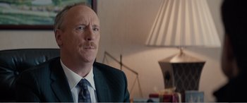 Movie still from “Office Christmas Party” (2016), directed by Will Speck – A man in a suit and tie sitting in front of a lamp; Close Up shot, Over the shoulder angle