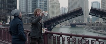 Movie still from “Office Christmas Party” (2016), directed by Will Speck – A man standing on a bridge eating a hot dog; Wide shot, Over the shoulder angle