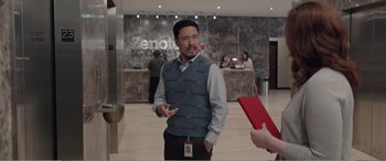 Movie still from “Office Christmas Party” (2016), directed by Will Speck – An asian man in a blue sweater talking to a woman; Medium shot, Over the shoulder angle