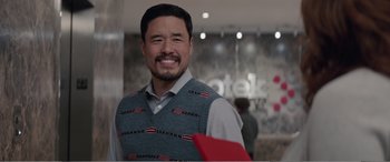 Movie still from “Office Christmas Party” (2016), directed by Will Speck – A man wearing a sweater vest smiles for the camera; Medium shot, Over the shoulder angle