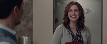 Movie still from “Office Christmas Party” (2016), directed by Will Speck – A woman with red curly hair smiles for the camera; Medium shot, Over the shoulder angle
