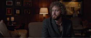 Movie still from “Office Christmas Party” (2016), directed by Will Speck – A man sitting on a couch in front of a lamp in a living room; Medium shot, Over the shoulder angle