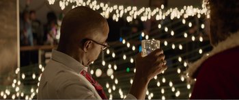 Movie still from “Office Christmas Party” (2016), directed by Will Speck – A man holding a glass of water in front of a string of christmas lights; Close Up shot, Low angle