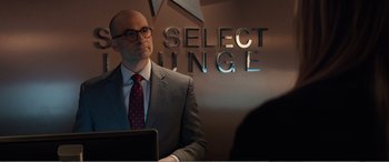 Movie still from “Office Christmas Party” (2016), directed by Will Speck – A man in a suit and tie standing in front of a sign; Medium shot, Over the shoulder angle