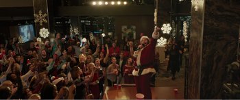 Movie still from “Office Christmas Party” (2016), directed by Will Speck – A man in a santa clause suit holding up a microphone; Wide shot, High angle