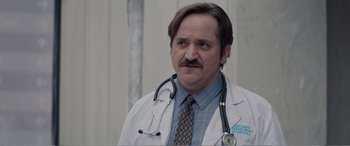 Movie still from “Office Christmas Party” (2016), directed by Will Speck – A man with a mustache wearing a doctor's coat and stethoscope around his neck; Close Up shot, Low angle