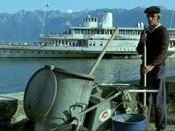 Movie still from “Oh, Woe Is Me” (1993), directed by Jean-Luc Godard – A man standing next to a boat on the water; Wide shot, Low angle