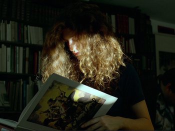 Movie still from “Oh, Woe Is Me” (1993), directed by Jean-Luc Godard – A woman is reading a book in a dark room; Medium shot, Low angle