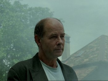 Movie still from “Oh, Woe Is Me” (1993), directed by Jean-Luc Godard – A man in a jacket is looking at the camera; Close Up shot, Low angle